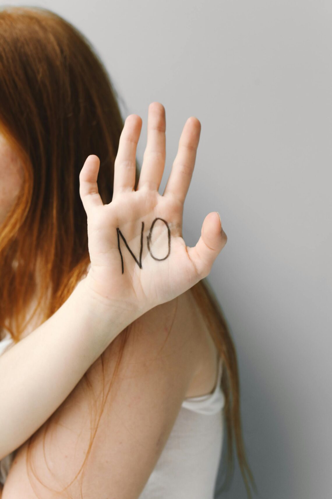 Teen girl raising her hand with “No” written on her palm, symbolizing refusal and strength against peer pressure