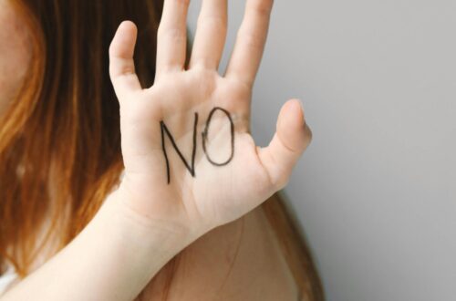 Teen girl raising her hand with “No” written on her palm, symbolizing refusal and strength against peer pressure